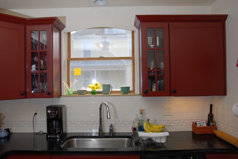 Photo of a mid-sized country kitchen in Other with an undermount sink, recessed-panel cabinets, red cabinets, soapstone benchtops, white splashback, ceramic splashback, stainless steel appliances and light hardwood floors.