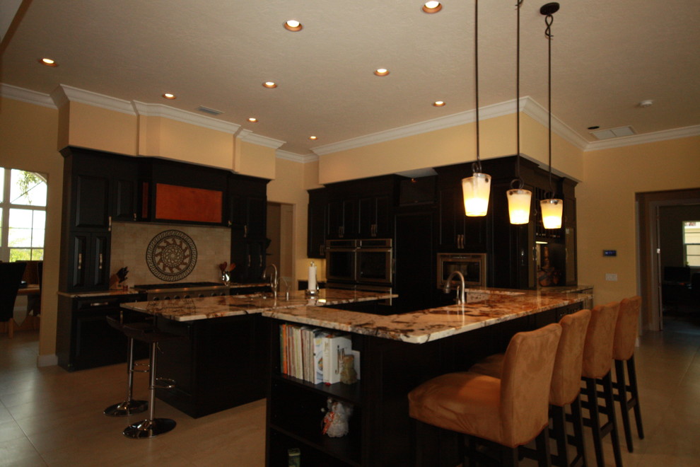 Example of a huge transitional u-shaped porcelain tile open concept kitchen design with raised-panel cabinets, black cabinets, beige backsplash, stainless steel appliances and an island