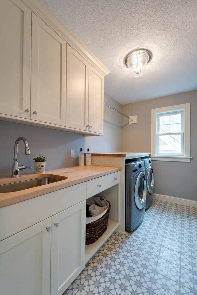 Inspiration for a transitional galley dedicated laundry room in Minneapolis with a single-bowl sink, white cabinets, wood benchtops, blue walls, ceramic floors, a side-by-side washer and dryer, multi-coloured floor and brown benchtop.
