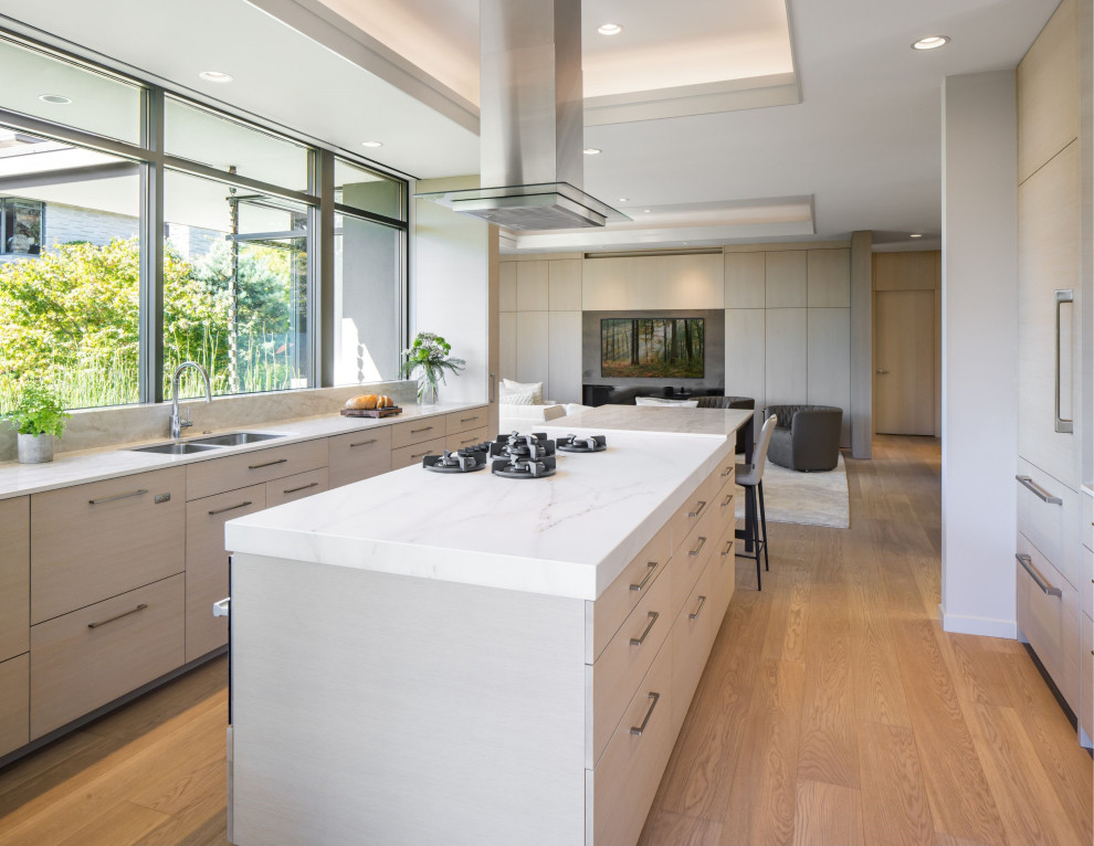Large contemporary galley open plan kitchen in Vancouver with a double-bowl sink, flat-panel cabinets, beige cabinets, engineered stone countertops, integrated appliances, light hardwood flooring, an island, beige floors, white worktops and a coffered ceiling.