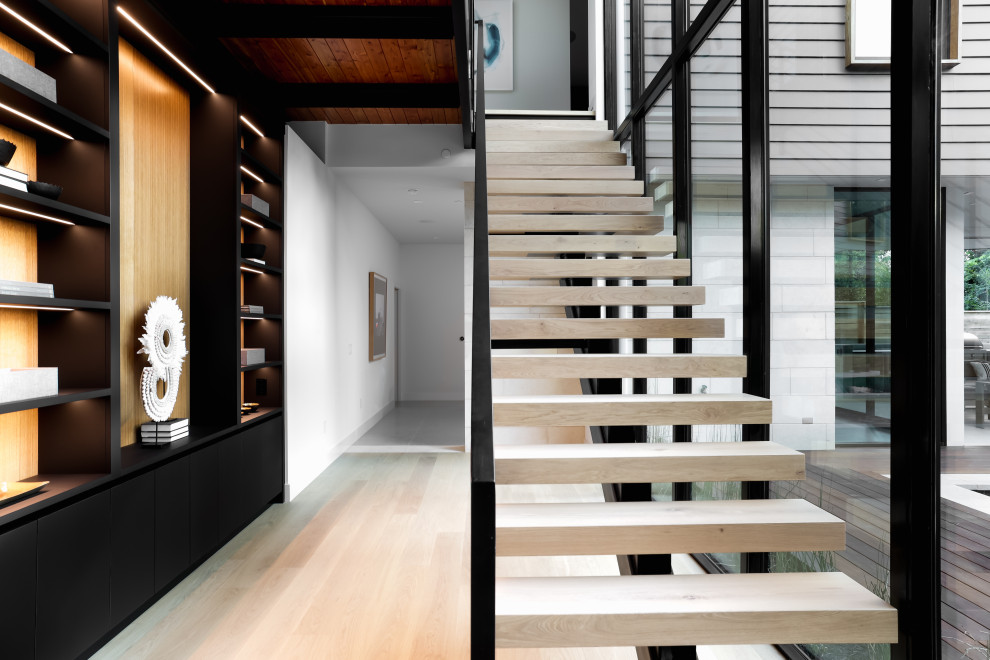 This is an example of a large contemporary wood floating staircase in Austin with wood risers, metal railing and wood walls.