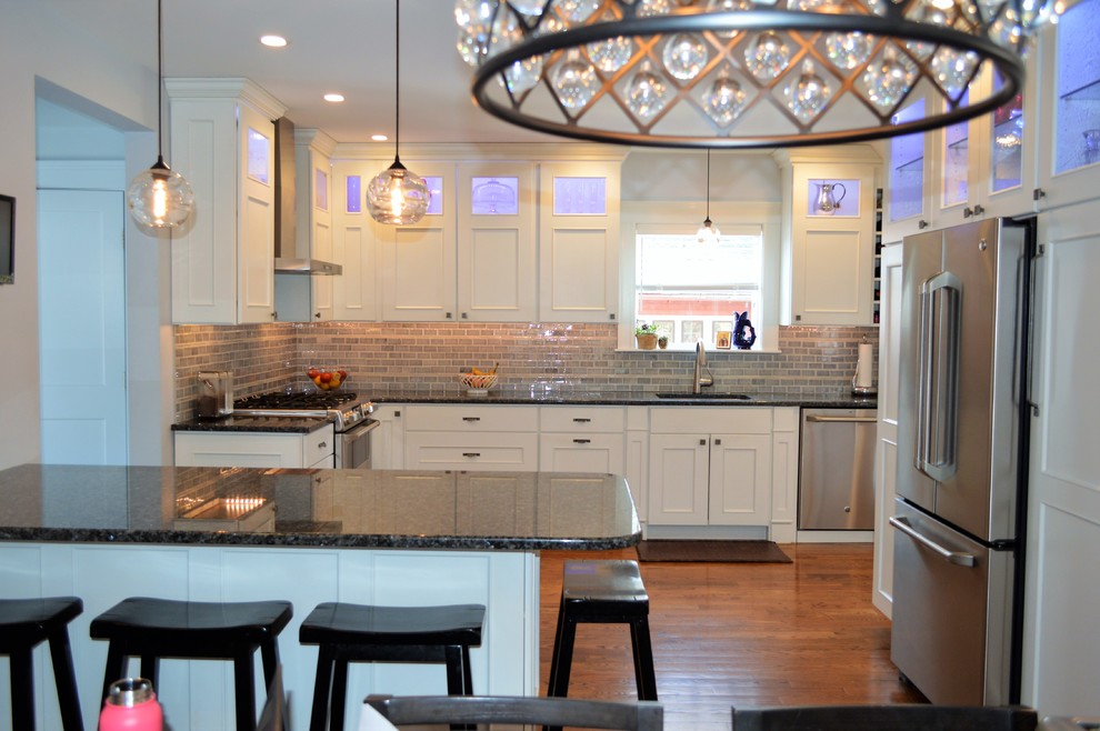 Example of a mid-sized transitional l-shaped medium tone wood floor eat-in kitchen design in Boston with an undermount sink, recessed-panel cabinets, white cabinets, granite countertops, gray backsplash, cement tile backsplash, stainless steel appliances, a peninsula and blue countertops