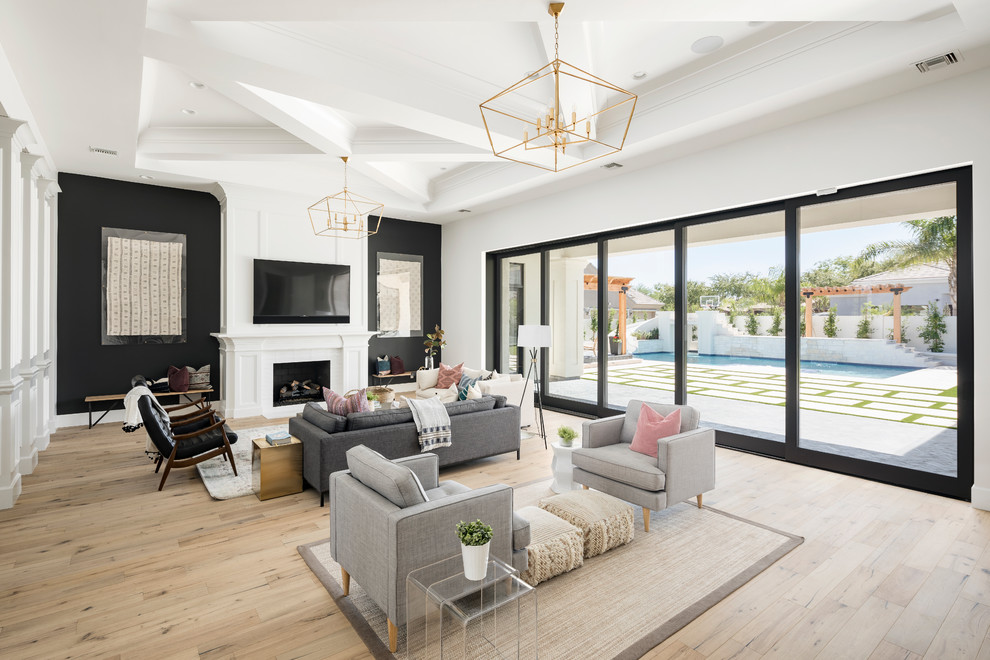 This is an example of a transitional open concept living room in Phoenix with black walls, light hardwood floors, a standard fireplace, a wall-mounted tv and beige floor.