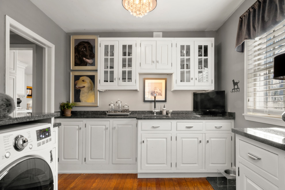 Exempel på en mellanstor klassisk grå u-formad grått tvättstuga, med en undermonterad diskho, luckor med upphöjd panel, vita skåp, bänkskiva i kvartsit, mellanmörkt trägolv, brunt golv, grå väggar och en tvättmaskin och torktumlare bredvid varandra