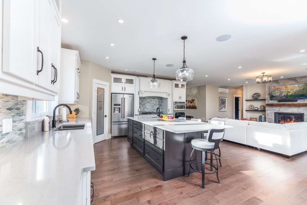 Mid-sized transitional medium tone wood floor and brown floor open concept kitchen photo with an undermount sink, shaker cabinets, white cabinets, granite countertops, gray backsplash, mosaic tile backsplash, stainless steel appliances, an island and gray countertops