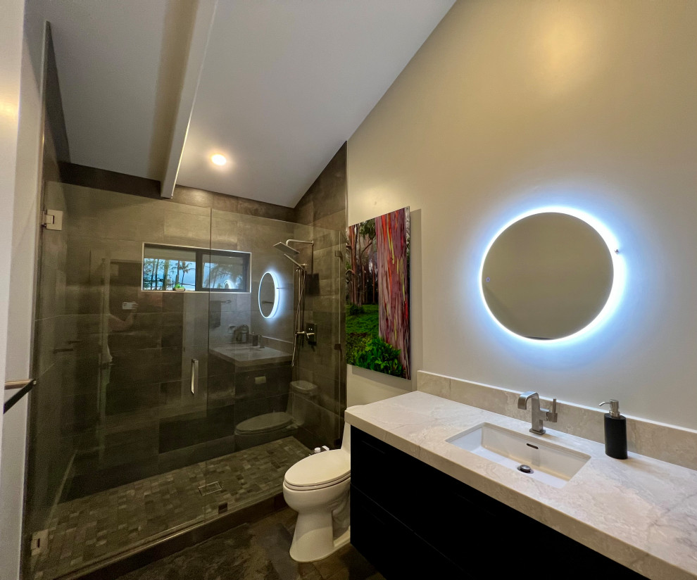 This is an example of an expansive modern 3/4 wet room bathroom in Hawaii with flat-panel cabinets, black cabinets, a bidet, gray tile, porcelain tile, white walls, porcelain floors, an undermount sink, engineered quartz benchtops, grey floor, a hinged shower door, grey benchtops, a single vanity, a floating vanity and exposed beam.