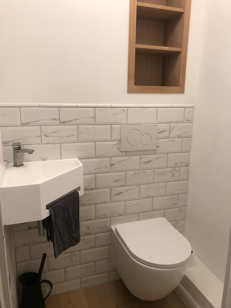 Inspiration för ett vit vitt toalett, med en vägghängd toalettstol, vit kakel, marmorkakel, vita väggar, ljust trägolv och ett väggmonterat handfat