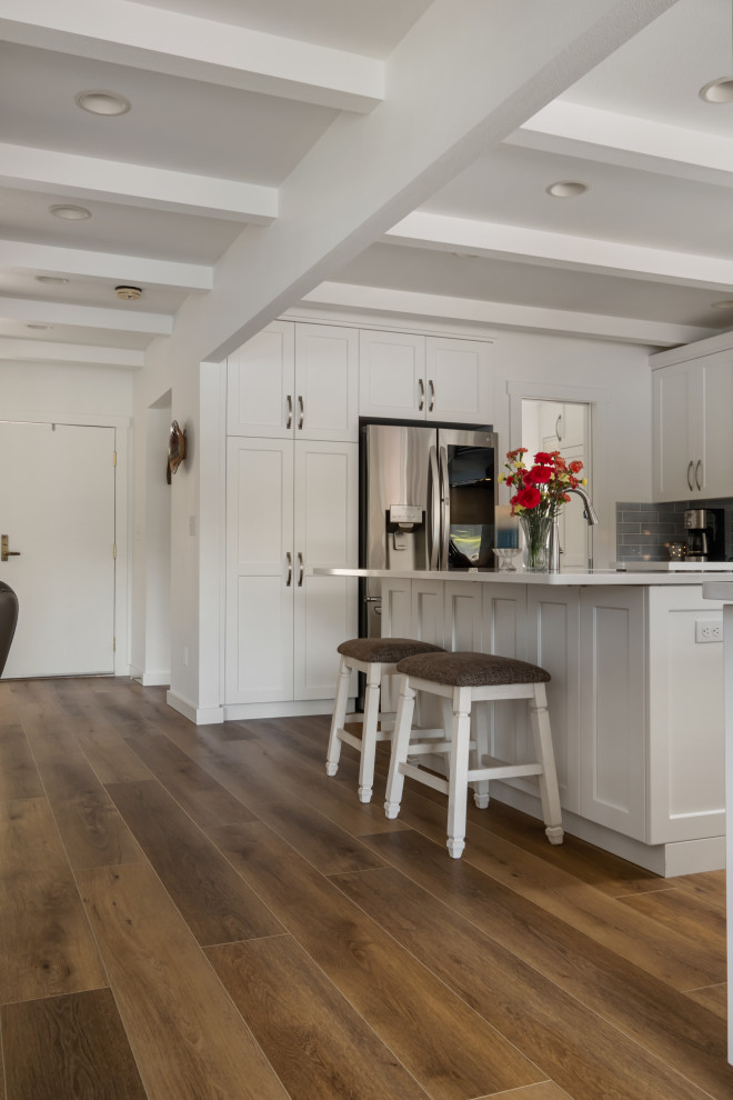 Photo of a medium sized beach style galley kitchen/diner in Seattle with a built-in sink, beaded cabinets, white cabinets, marble worktops, grey splashback, ceramic splashback, stainless steel appliances, vinyl flooring, multiple islands, brown floors, white worktops and a coffered ceiling.
