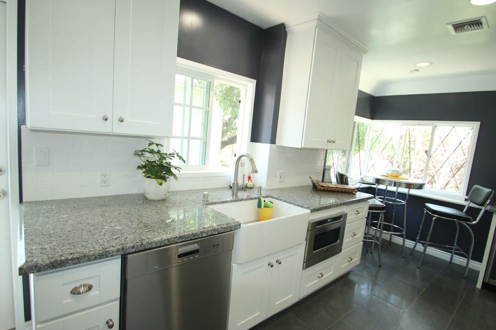 Mid-sized traditional u-shaped separate kitchen in Los Angeles with a farmhouse sink, white cabinets, granite benchtops, white splashback, subway tile splashback, stainless steel appliances, porcelain floors and no island.