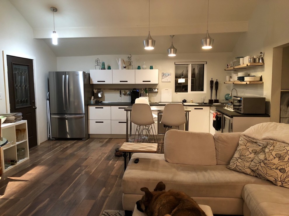 Small modern l-shaped open plan kitchen in San Francisco with a farmhouse sink, flat-panel cabinets, white cabinets, laminate benchtops, white splashback, metal splashback, stainless steel appliances, medium hardwood floors, with island, brown floor and grey benchtop.