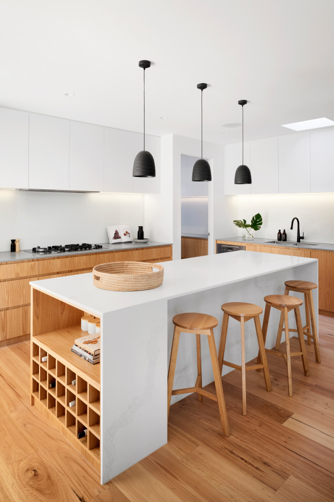 Inspiration for a mid-sized contemporary l-shaped open plan kitchen in Melbourne with an undermount sink, flat-panel cabinets, medium wood cabinets, quartz benchtops, white splashback, black appliances, medium hardwood floors, with island, brown floor and white benchtop.