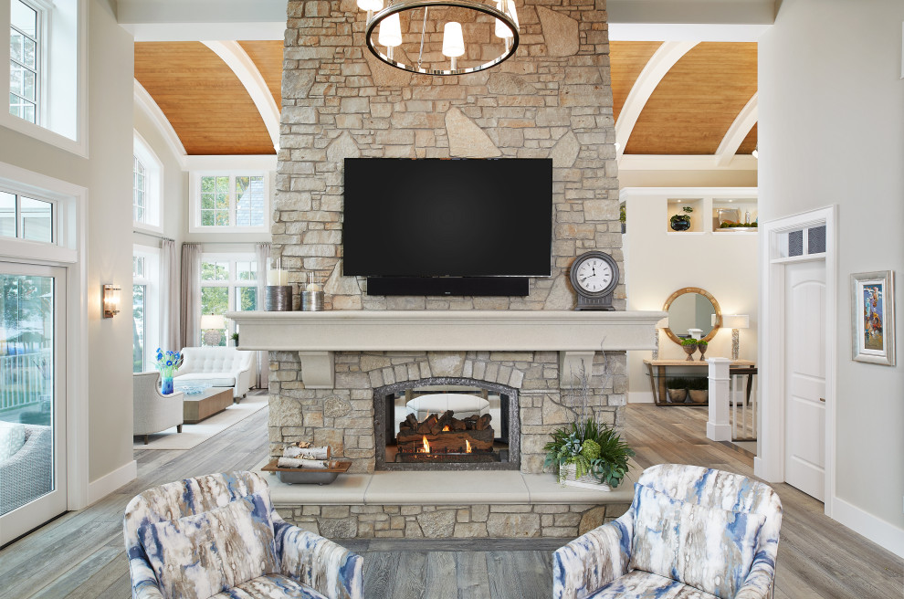 Inspiration for a large beach style open concept living room in Grand Rapids with grey walls, light hardwood floors, a two-sided fireplace, a wall-mounted tv, grey floor and vaulted.