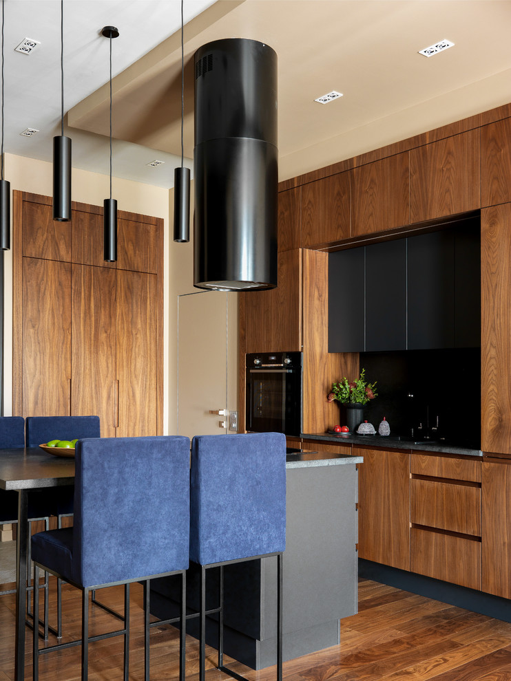 Photo of a contemporary l-shaped kitchen in Moscow with flat-panel cabinets, medium wood cabinets, black splashback, black appliances, dark hardwood floors, with island, brown floor and grey benchtop.