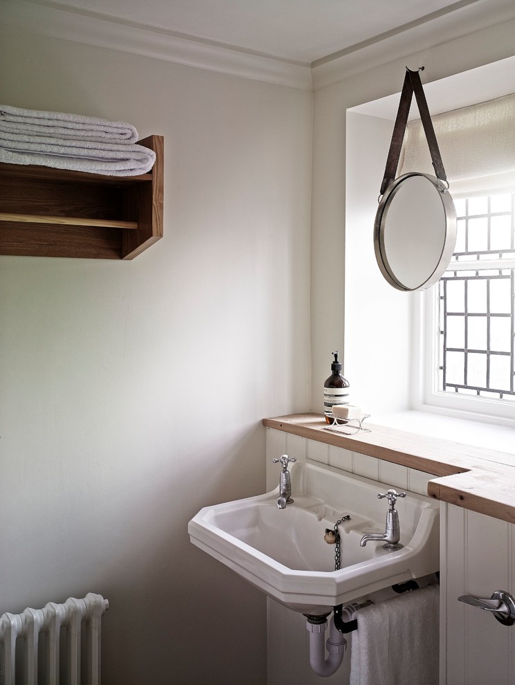This is an example of a small country bathroom in Sussex with a wall-mount sink and wood benchtops.
