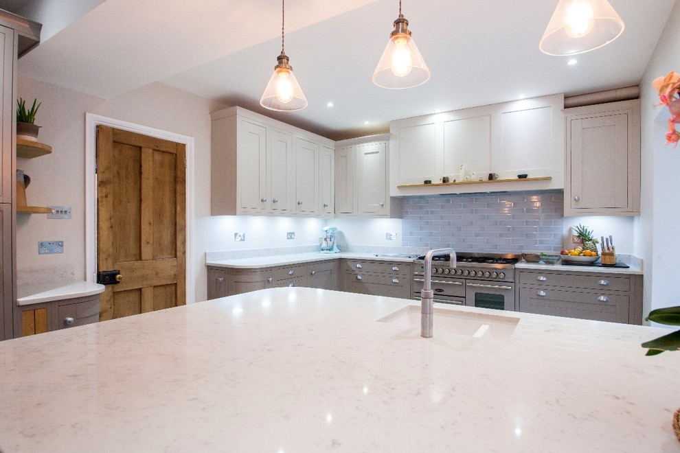 This is an example of a large transitional u-shaped open plan kitchen in Hampshire with a drop-in sink, shaker cabinets, grey cabinets, quartzite benchtops, blue splashback, ceramic splashback, panelled appliances, ceramic floors, with island and beige floor.