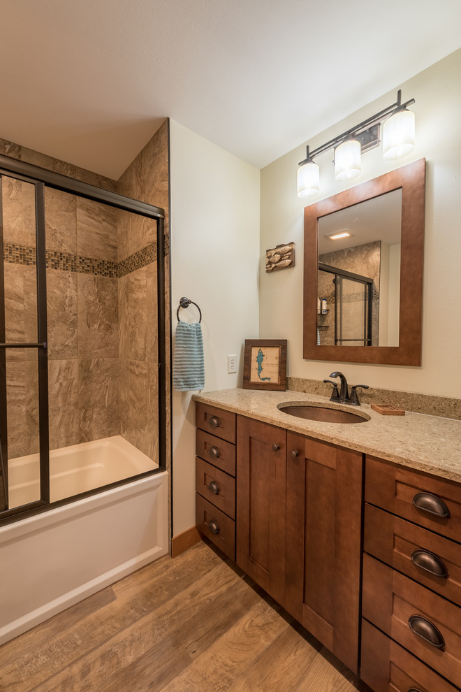 Photo of a small country 3/4 bathroom in Minneapolis with shaker cabinets, medium wood cabinets, an alcove tub, a shower/bathtub combo, brown tile, ceramic tile, beige walls, medium hardwood floors, an undermount sink, granite benchtops, brown floor, a sliding shower screen and beige benchtops.
