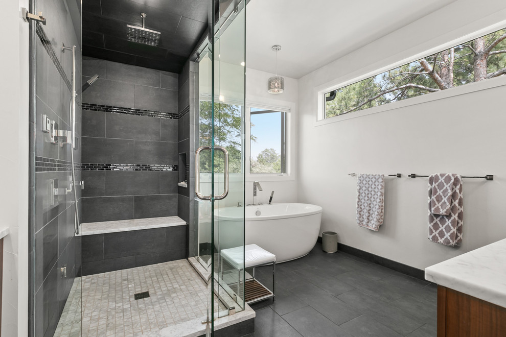 Mid-sized contemporary master bathroom in Denver with flat-panel cabinets, medium wood cabinets, a freestanding tub, a corner shower, gray tile, stone tile, white walls, ceramic floors, a drop-in sink, engineered quartz benchtops, grey floor, a hinged shower door and grey benchtops.