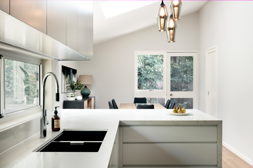 Large contemporary l-shaped eat-in kitchen in Sydney with an undermount sink, grey cabinets, quartz benchtops, window splashback, stainless steel appliances, medium hardwood floors, a peninsula, brown floor and multi-coloured benchtop.