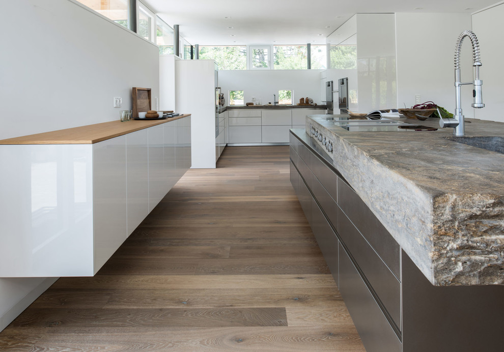 Photo of a large contemporary l-shaped eat-in kitchen in Munich with an integrated sink, flat-panel cabinets, white cabinets, limestone benchtops, white splashback and with island.