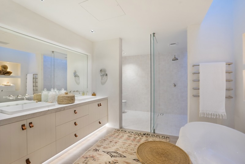 Beach style master bathroom in Central Coast with white cabinets, a freestanding tub, an open shower, white tile, white walls, light hardwood floors, a drop-in sink, beige floor and an open shower.