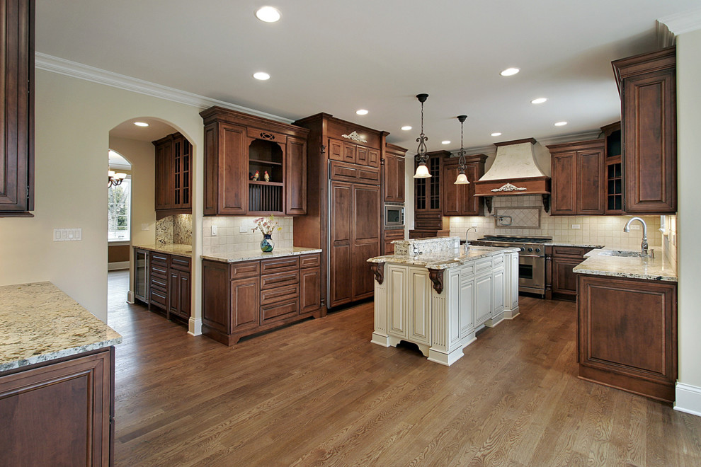 Example of a classic u-shaped eat-in kitchen design in Philadelphia with an undermount sink, raised-panel cabinets, brown cabinets, granite countertops, beige backsplash, stone tile backsplash and stainless steel appliances