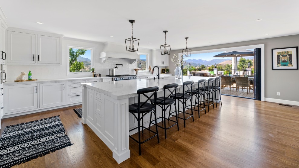 Large transitional single-wall medium tone wood floor and brown floor eat-in kitchen photo with a single-bowl sink, raised-panel cabinets, white cabinets, quartzite countertops, white backsplash, ceramic backsplash, stainless steel appliances, an island and white countertops