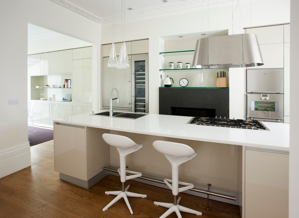 Photo of a contemporary kitchen in London with a double-bowl sink, flat-panel cabinets, white cabinets, beige splashback, medium hardwood floors and with island.