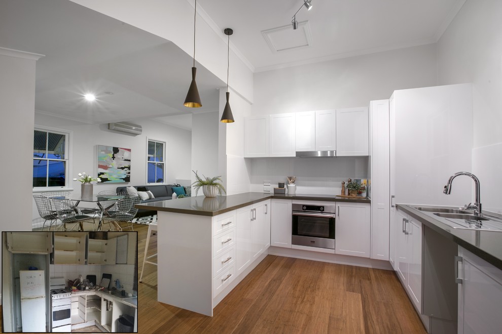 This is an example of a modern u-shaped eat-in kitchen in Brisbane with a double-bowl sink, recessed-panel cabinets, white cabinets, quartz benchtops, white splashback, ceramic splashback, stainless steel appliances and bamboo floors.
