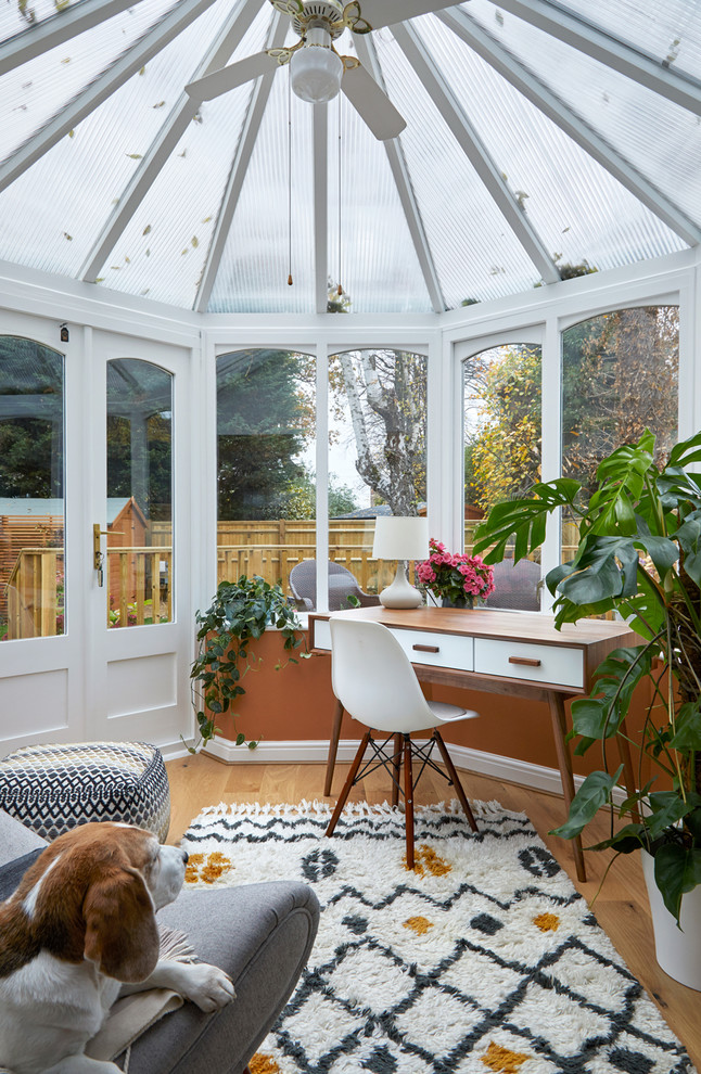 Photo of a transitional sunroom in London with light hardwood floors, a glass ceiling and beige floor.