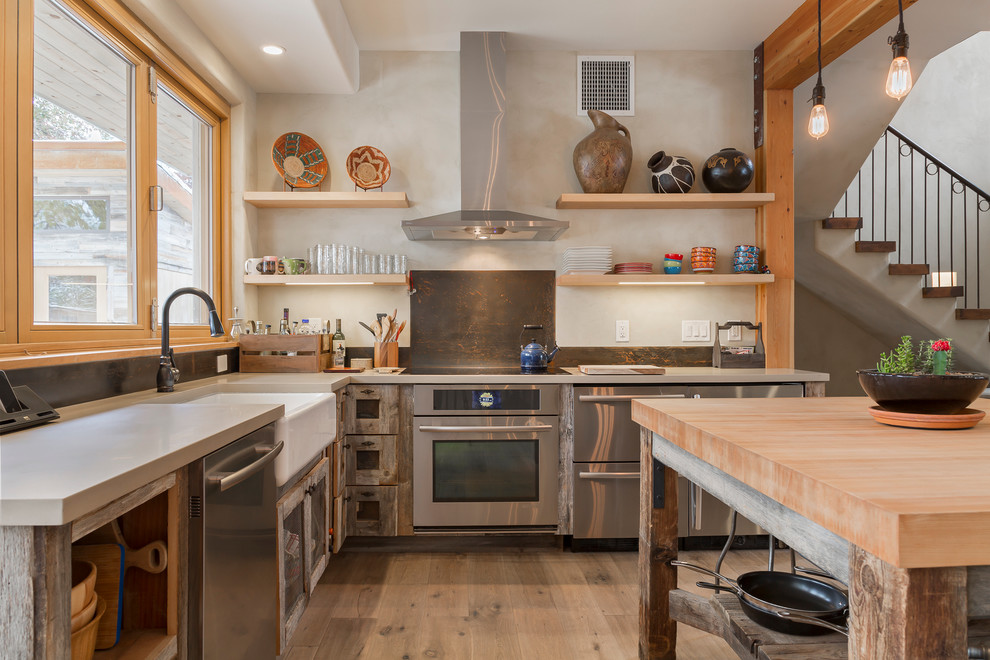 Contemporary l-shaped eat-in kitchen in Denver with a farmhouse sink, distressed cabinets, brown splashback, metal splashback and stainless steel appliances.