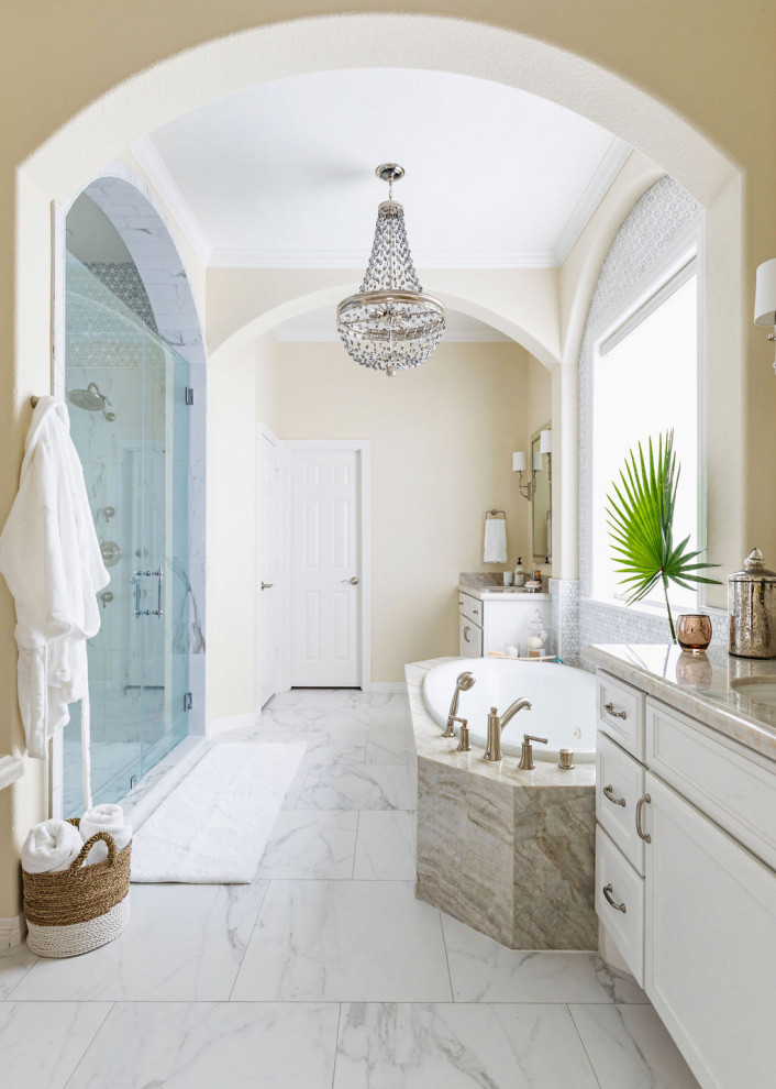 Photo of a transitional master bathroom in Houston with recessed-panel cabinets, white cabinets, a drop-in tub, an alcove shower, multi-coloured tile, beige walls, an undermount sink, a hinged shower door, beige benchtops, an enclosed toilet, a double vanity and a built-in vanity.