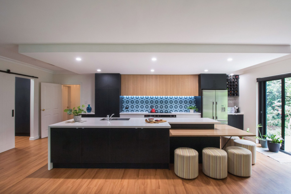 Design ideas for a large contemporary galley open plan kitchen in Adelaide with a double-bowl sink, flat-panel cabinets, black cabinets, engineered stone countertops, blue splashback, cement tile splashback, stainless steel appliances, laminate floors, an island, brown floors, white worktops and a drop ceiling.