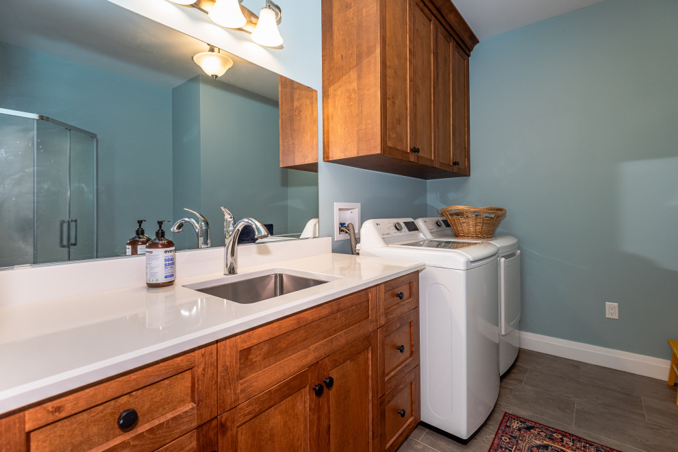 Inspiration for a galley dedicated laundry room in Toronto with an undermount sink, recessed-panel cabinets, medium wood cabinets, blue walls, ceramic floors, a side-by-side washer and dryer, brown floor and white benchtop.