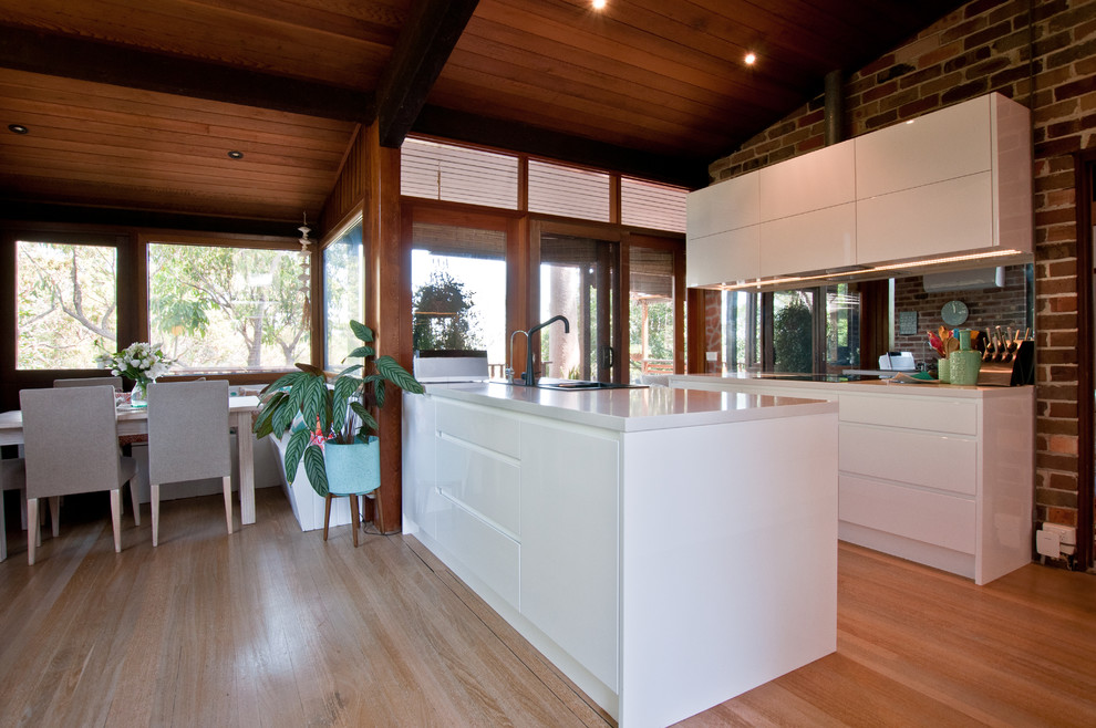 Inspiration for a mid-sized eclectic u-shaped eat-in kitchen in Sydney with a drop-in sink, flat-panel cabinets, white cabinets, quartzite benchtops, glass sheet splashback, stainless steel appliances, dark hardwood floors and a peninsula.