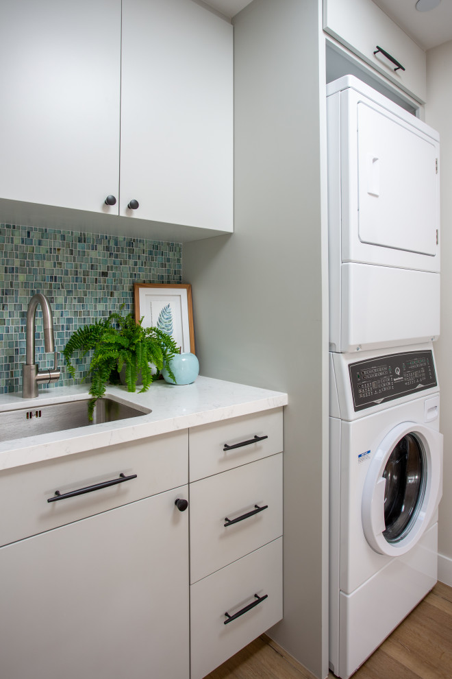 Design ideas for a small beach style u-shaped dedicated laundry room in Santa Barbara with an undermount sink, flat-panel cabinets, grey cabinets, quartz benchtops, blue splashback, mosaic tile splashback, grey walls, vinyl floors, a stacked washer and dryer, beige floor, white benchtop and vaulted.