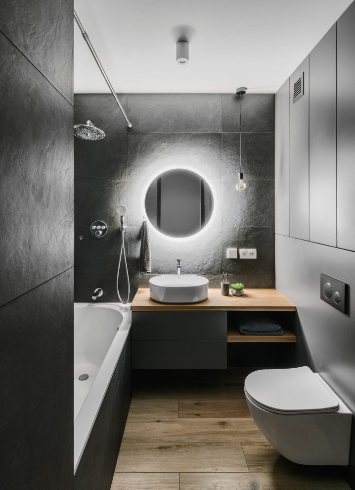 This is an example of a medium sized contemporary grey and white ensuite bathroom in Moscow with flat-panel cabinets, grey cabinets, a submerged bath, a shower/bath combination, a wall mounted toilet, grey tiles, ceramic tiles, grey walls, porcelain flooring, a built-in sink, wooden worktops, brown floors, a shower curtain, beige worktops, an enclosed toilet, a single sink and a floating vanity unit.