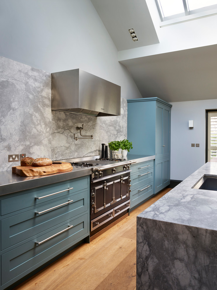 Inspiration for a large transitional u-shaped separate kitchen in London with an undermount sink, recessed-panel cabinets, blue cabinets, solid surface benchtops, grey splashback, stone slab splashback, stainless steel appliances, medium hardwood floors, with island and brown floor.
