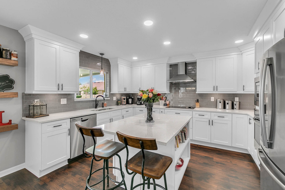 Inspiration for a mid-sized transitional u-shaped eat-in kitchen in Orlando with a double-bowl sink, shaker cabinets, white cabinets, quartz benchtops, grey splashback, glass tile splashback, stainless steel appliances, laminate floors, with island, brown floor and white benchtop.