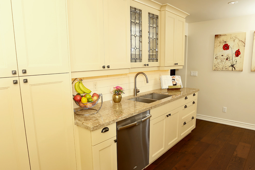 Example of a small transitional galley medium tone wood floor and brown floor enclosed kitchen design in Toronto with a double-bowl sink, shaker cabinets, beige cabinets, quartz countertops, beige backsplash, ceramic backsplash, stainless steel appliances and a peninsula