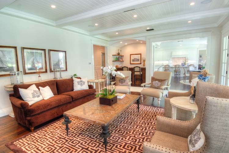 This is an example of a beach style open concept living room in Orange County with white walls, medium hardwood floors, a standard fireplace, a wood fireplace surround and a concealed tv.