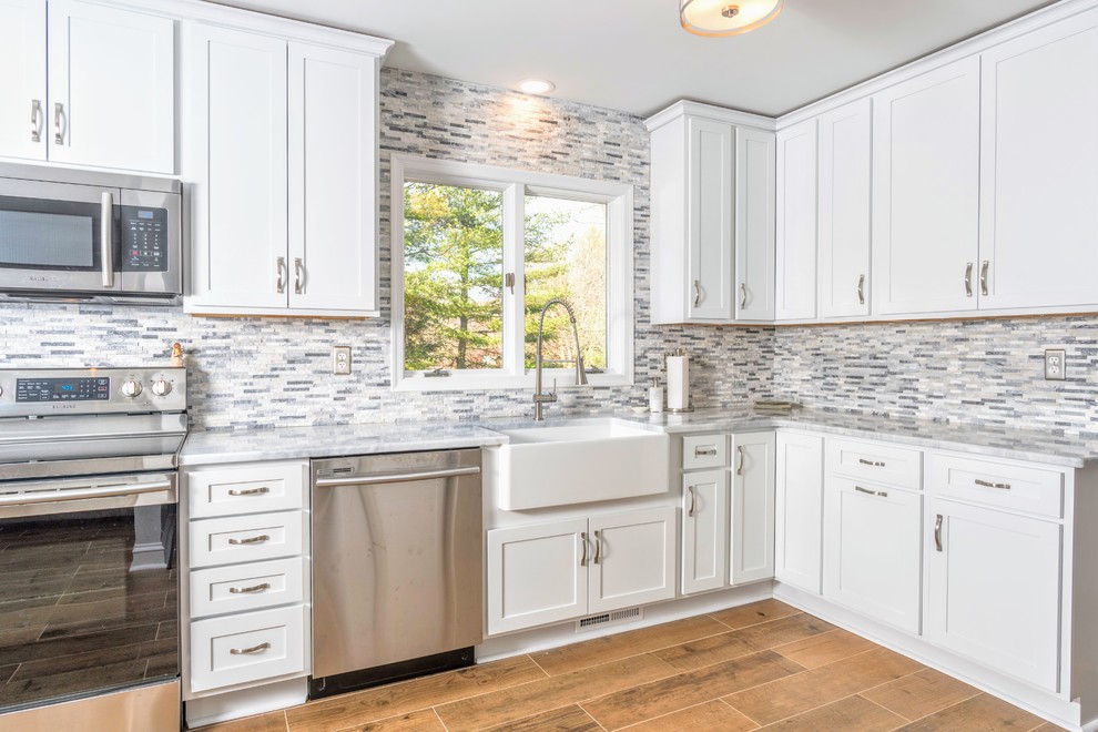 Eat-in kitchen - large transitional l-shaped ceramic tile and brown floor eat-in kitchen idea in Baltimore with a farmhouse sink, shaker cabinets, white cabinets, granite countertops, gray backsplash, stone tile backsplash, stainless steel appliances, no island and white countertops