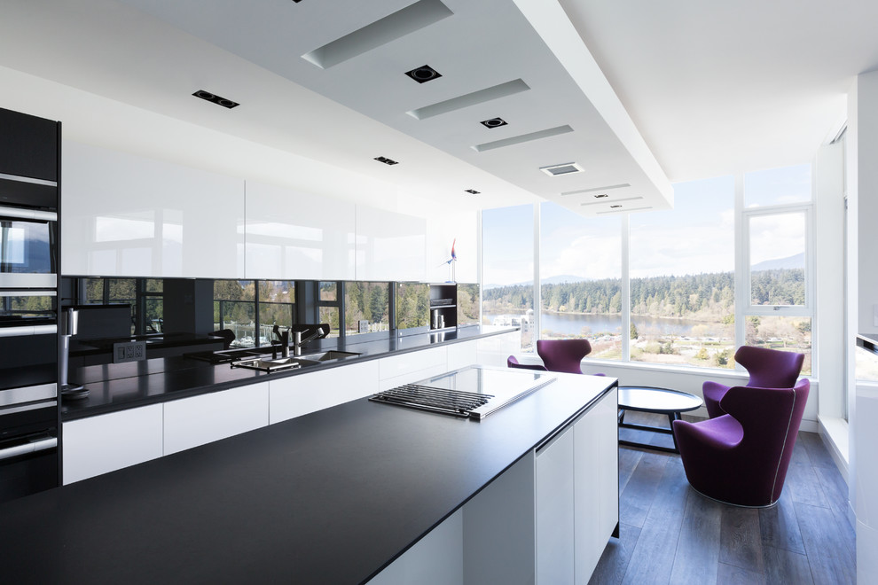 Large contemporary single-wall eat-in kitchen in Vancouver with a double-bowl sink, flat-panel cabinets, white cabinets, solid surface benchtops, black splashback, glass sheet splashback, panelled appliances, medium hardwood floors, with island, grey floor and black benchtop.