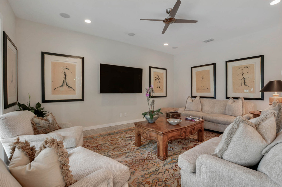 This is an example of a large transitional open concept family room in Tampa with a library, white walls, light hardwood floors, a wall-mounted tv and beige floor.