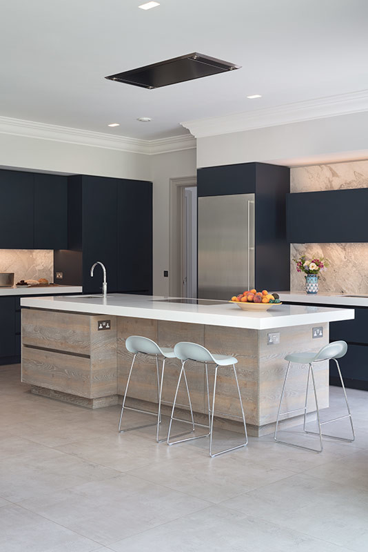 Large contemporary l-shaped open plan kitchen in London with flat-panel cabinets, blue cabinets, solid surface benchtops, beige splashback, marble splashback, stainless steel appliances, with island and white benchtop.