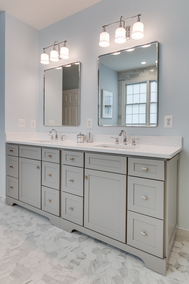 This is an example of a mid-sized transitional master bathroom in DC Metro with shaker cabinets, grey cabinets, a freestanding tub, a corner shower, a one-piece toilet, white tile, marble, blue walls, marble floors, an undermount sink, engineered quartz benchtops, white floor, a hinged shower door and white benchtops.