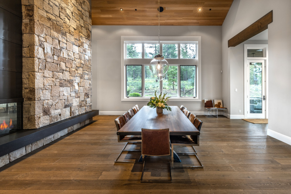 Aménagement d'une grande salle à manger classique avec un mur gris, un sol en bois brun, une cheminée double-face, un manteau de cheminée en métal, un sol marron et un plafond en bois.
