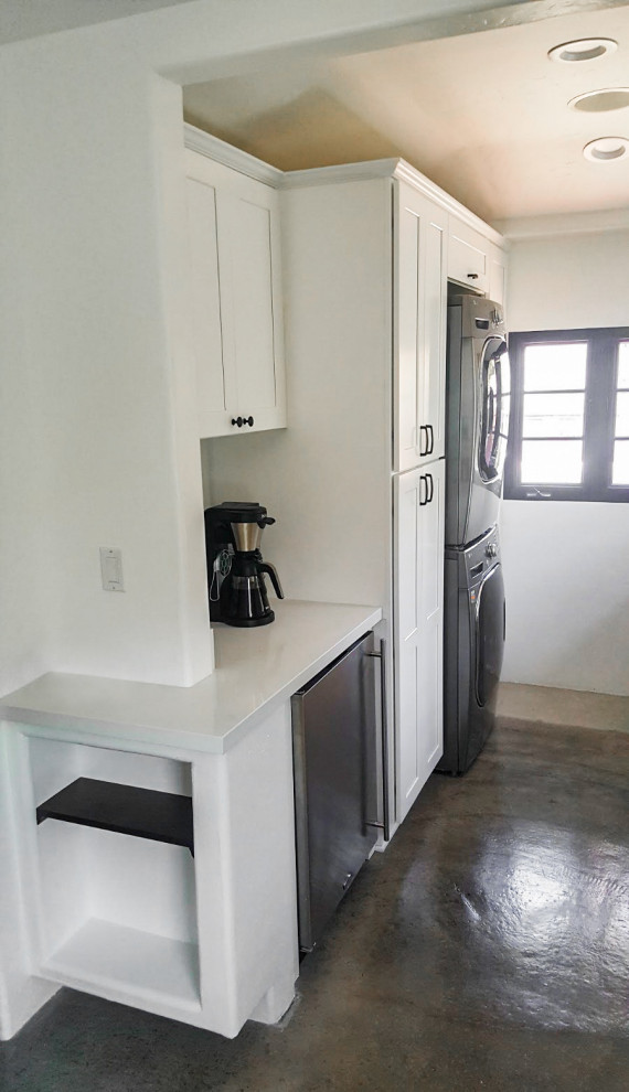 Example of a mid-sized transitional galley concrete floor and multicolored floor kitchen pantry design in Los Angeles with a farmhouse sink, shaker cabinets, white cabinets, quartz countertops, white backsplash, subway tile backsplash, stainless steel appliances, a peninsula and white countertops