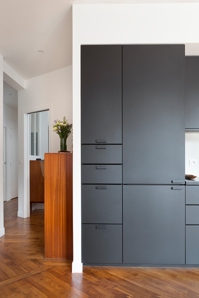 This is an example of a mid-sized contemporary l-shaped eat-in kitchen in Paris with an undermount sink, black cabinets, laminate benchtops, medium hardwood floors and black benchtop.
