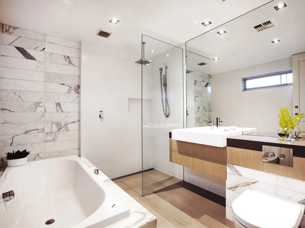 Mid-sized contemporary master bathroom in Melbourne with flat-panel cabinets, light wood cabinets, a drop-in tub, a curbless shower, a wall-mount toilet, marble, white walls, ceramic floors, stainless steel benchtops, beige floor, an open shower, gray tile, black benchtops and a vessel sink.
