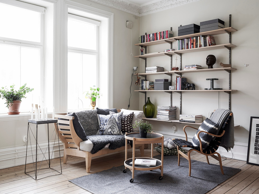 This is an example of a mid-sized scandinavian enclosed living room in Gothenburg with a library, beige walls, light hardwood floors, no fireplace and no tv.